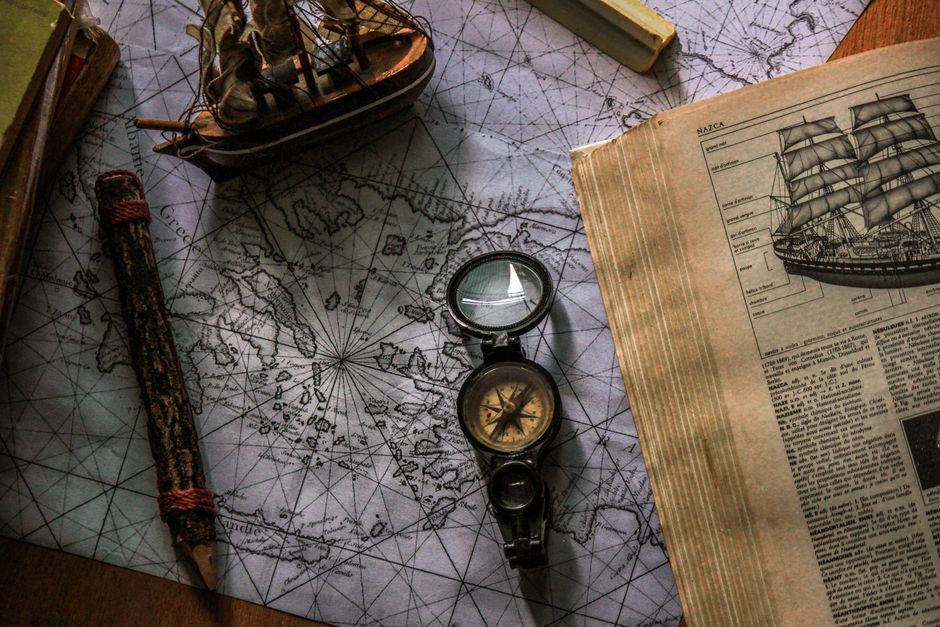 Old map and compass with book and ship model, evoking travel and exploration.
